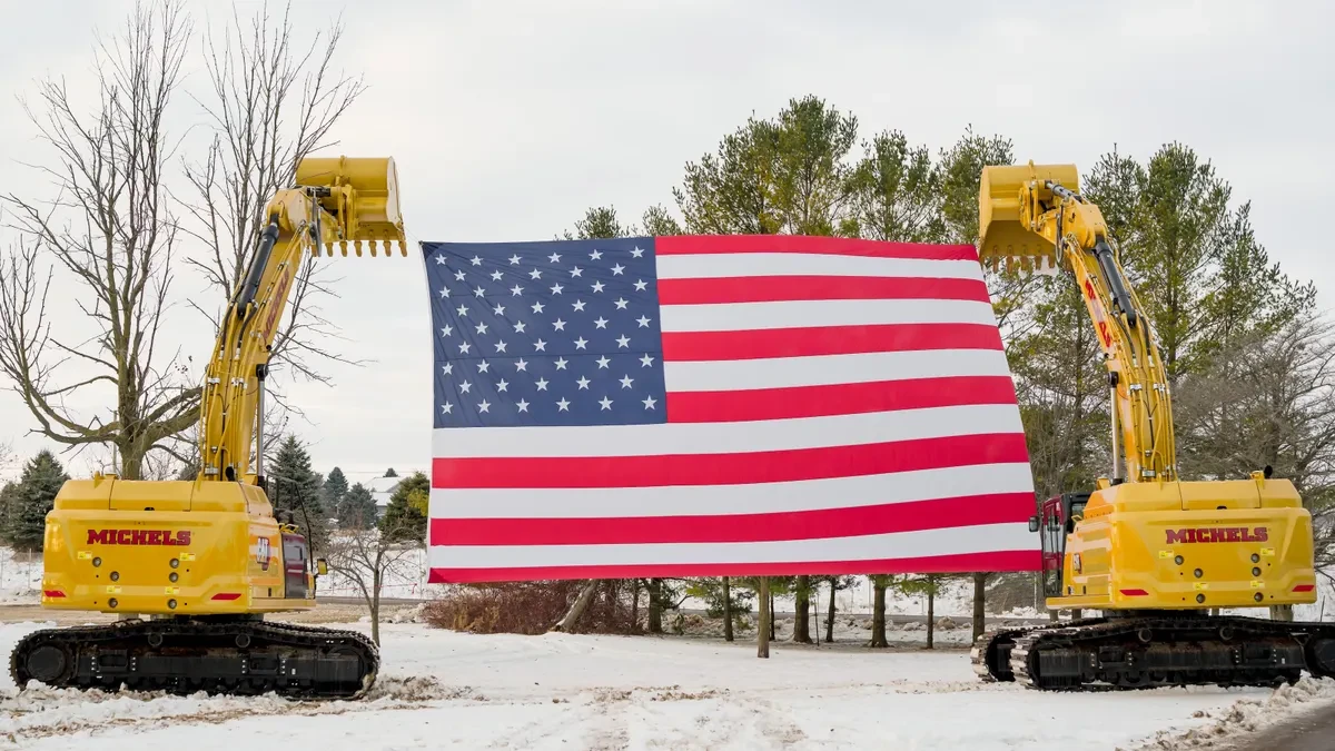 Two construction machines outside suspending a US flag between them.