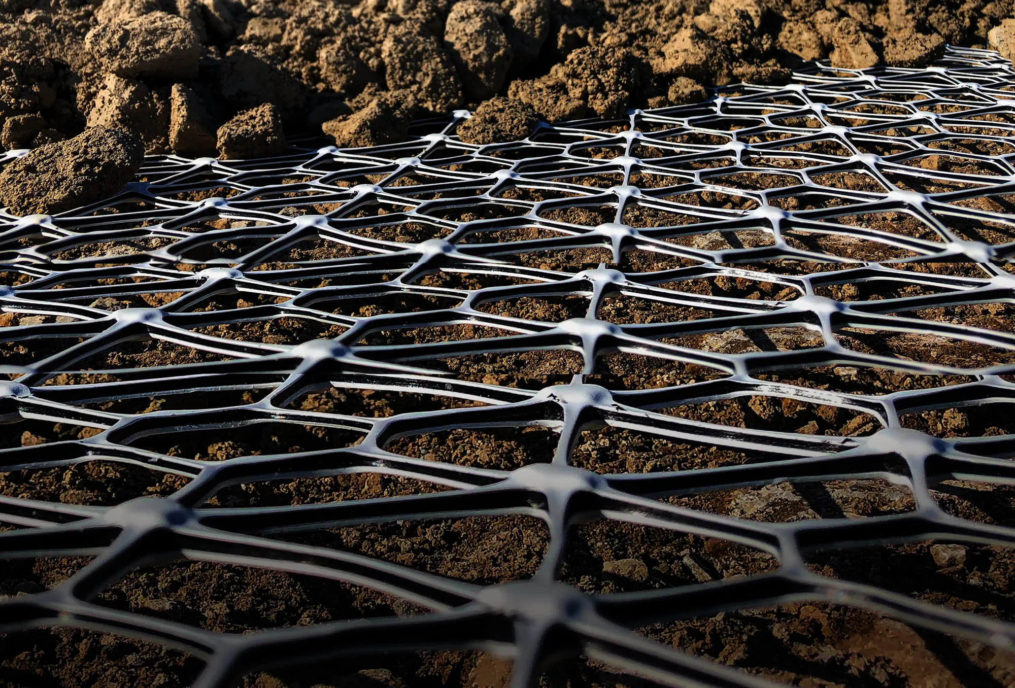 Tensar's InterAx geogrid laid on the ground at a job site with dirt and aggregate material visible.