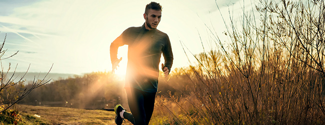 Man in athletic clothing running with sun setting in the background.