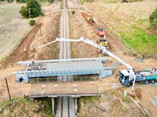A prefabricated modular bridge segment being lowered into place over a railroad track.