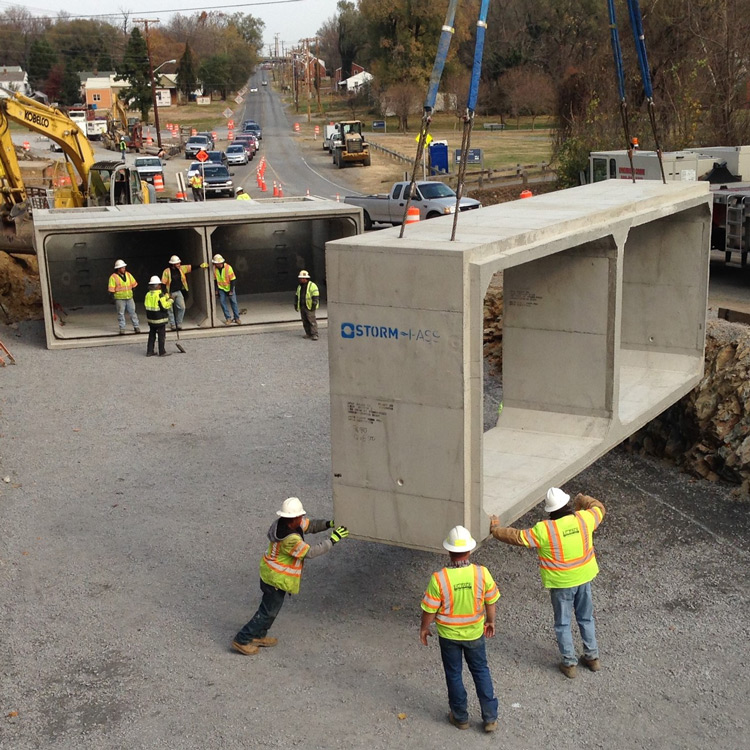 Workers in high-visibility vests and hardhats helping arrange precast concrete structures suspended by a crane at a job site.